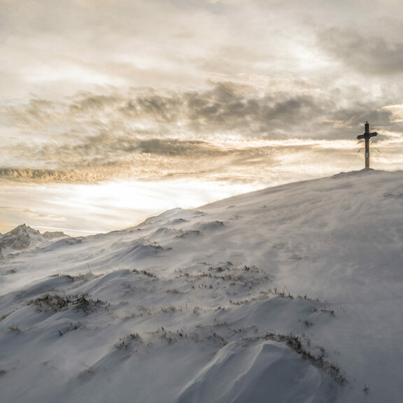 silhouette-of-brown-cross-on-mountain-covered-with-snow-under-white-clouds